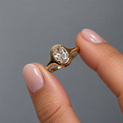 1.5 ct oval-cut moissanite bezel-prong ring in 18k yellow gold vermeil, held between two fingertips