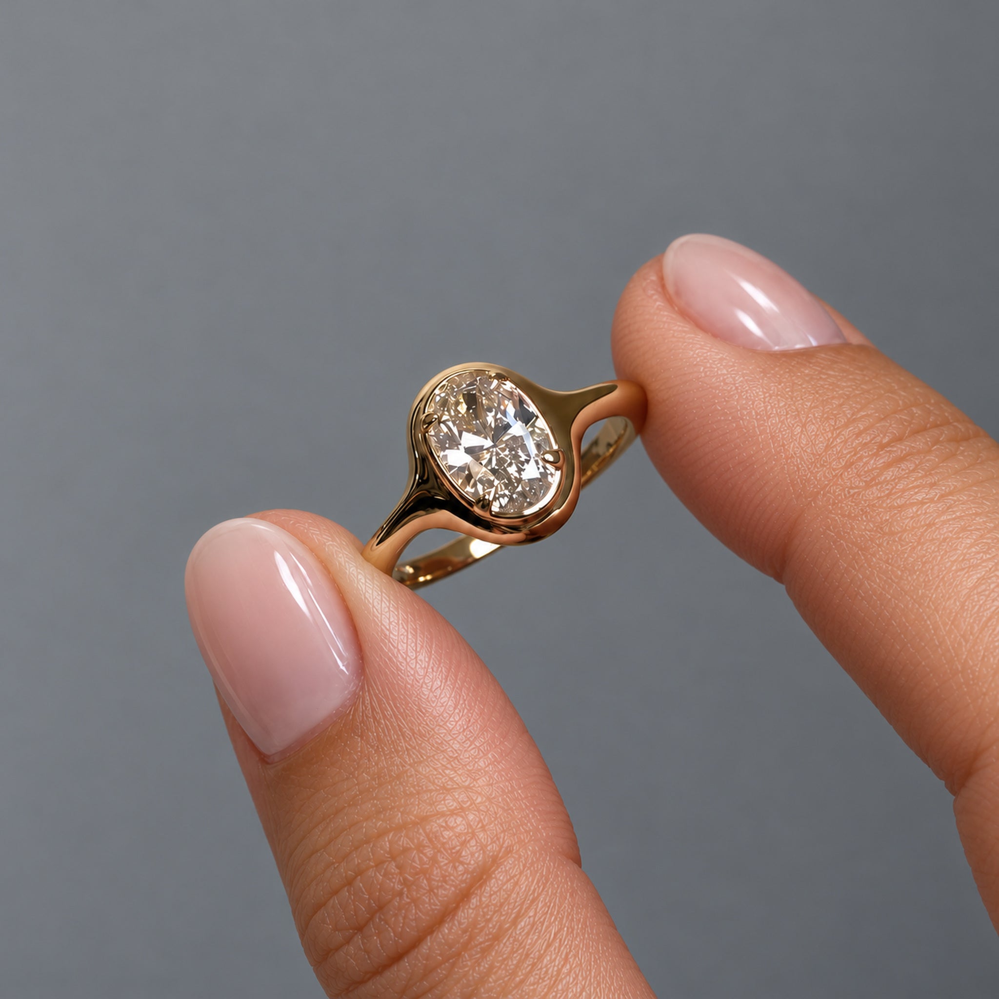 1.5 ct oval-cut moissanite bezel-prong ring in 18k yellow gold vermeil, held between two fingertips