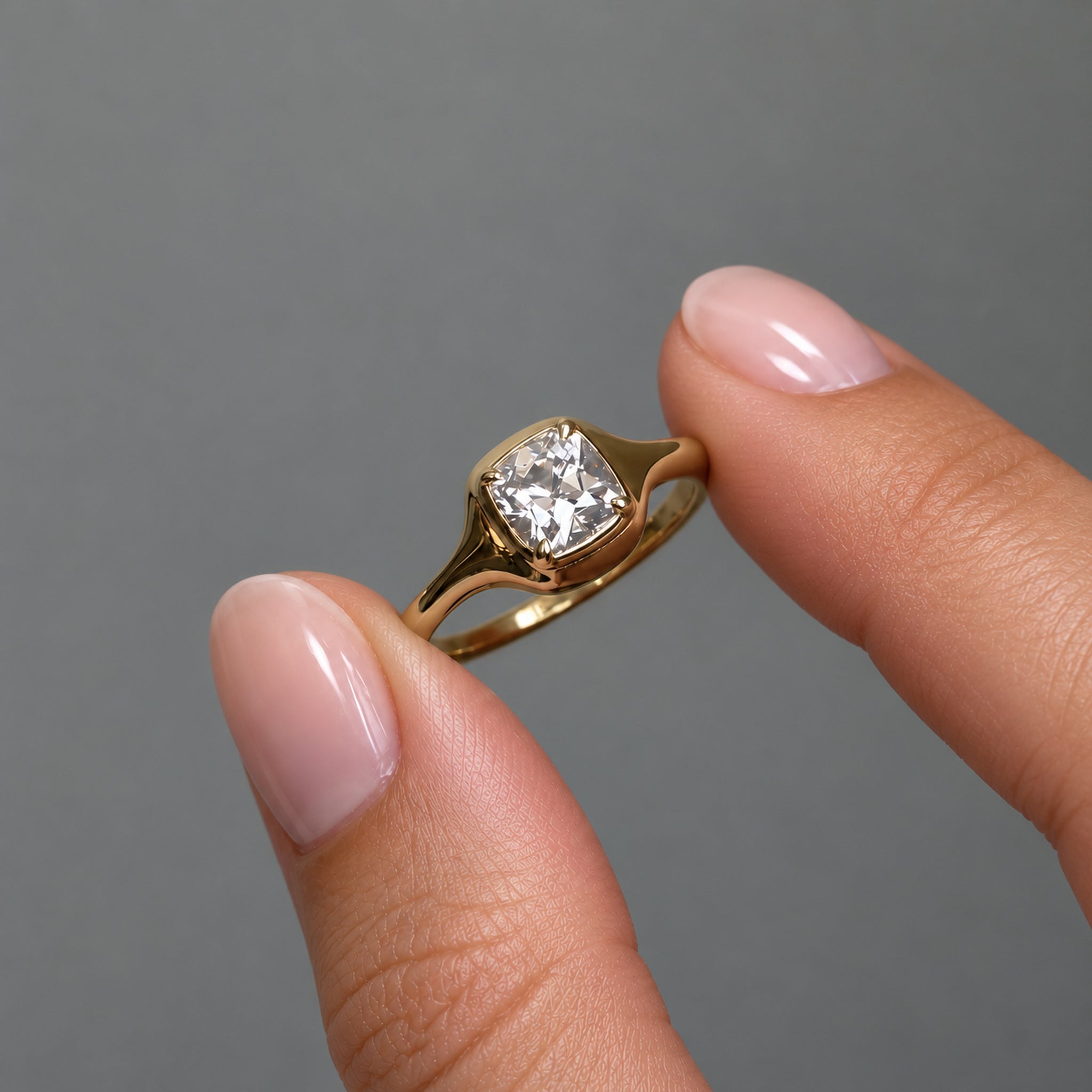 1 ct cushion-cut moissanite bezel-prong ring in 18k yellow gold vermeil, held between two fingertips
