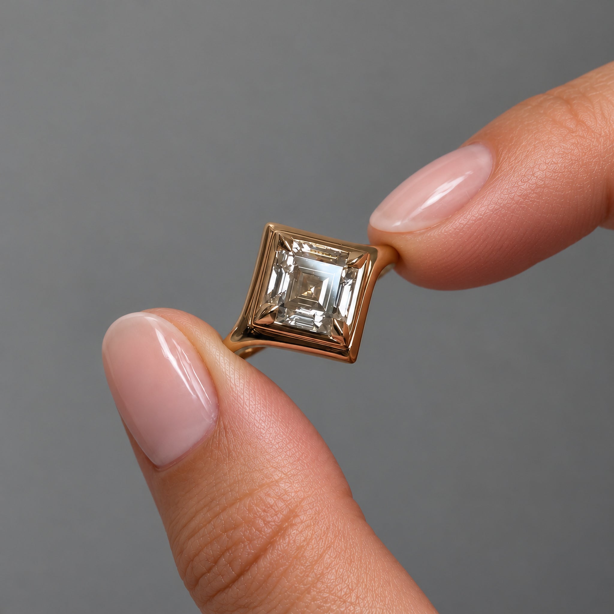 1 ct diagonal asscher-cut moissanite bezel-prong ring in 18k yellow gold vermeil, held between two fingertips