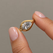 2 ct east-west pear-cut moissanite bezel-prong ring in 18k yellow gold vermeil, held between two fingertips