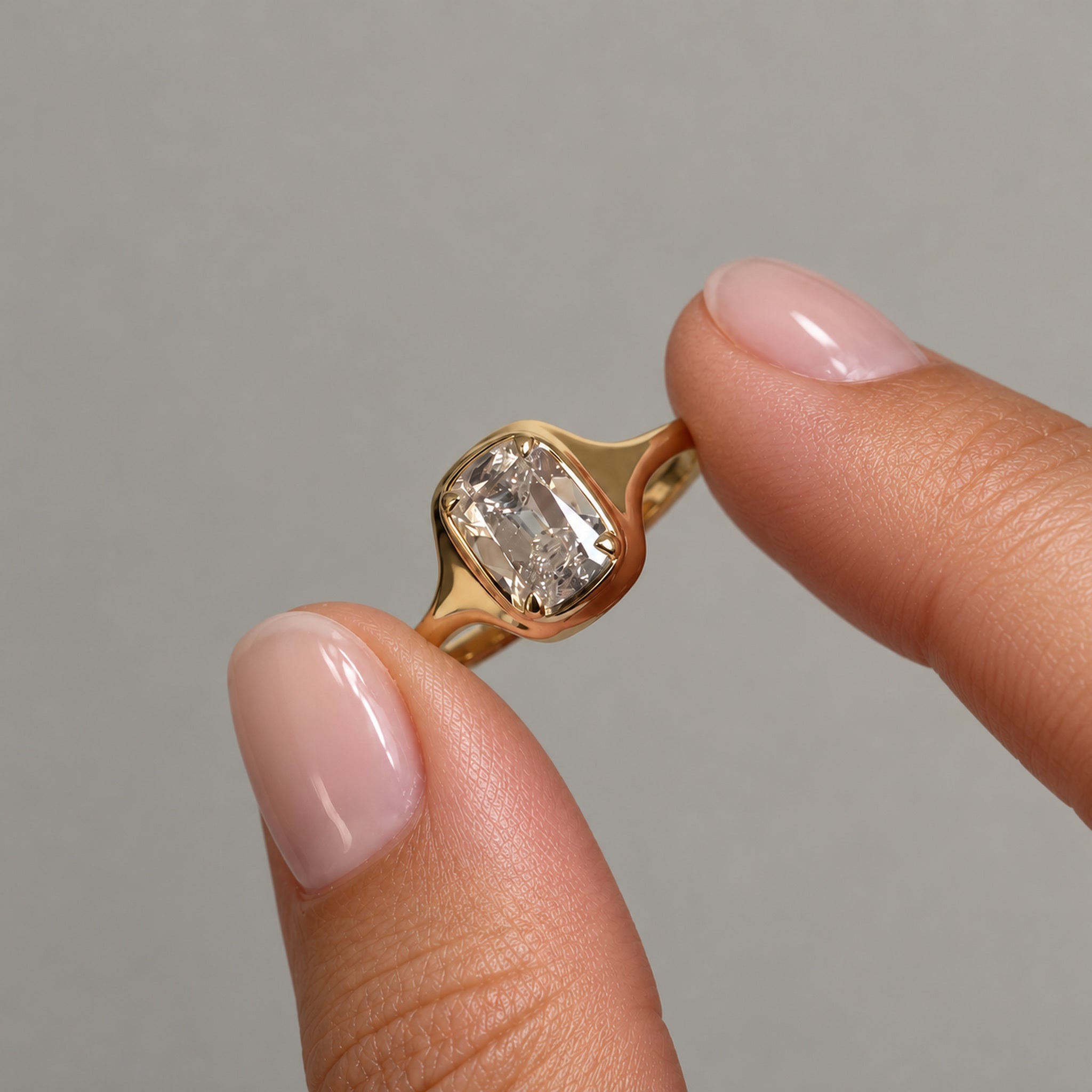 2 ct elongated cushion-cut moissanite bezel-prong ring in 18k yellow gold vermeil, held between two fingertips