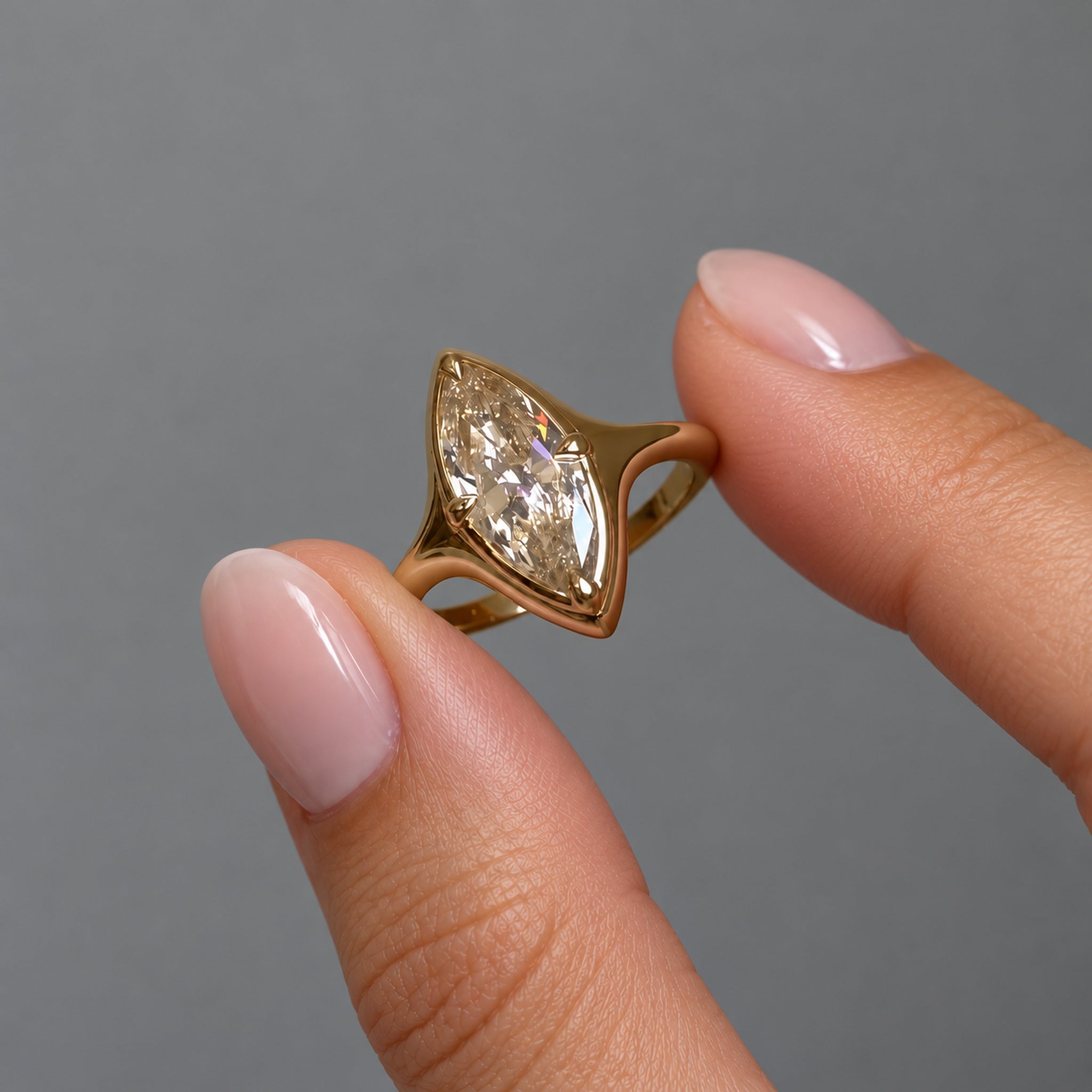 2 ct marquise-cut moissanite bezel-prong ring in 18k yellow gold vermeil, held between two fingertips