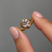 2 ct round-cut moissanite bezel-prong ring in 18k yellow gold vermeil, held between two fingertips