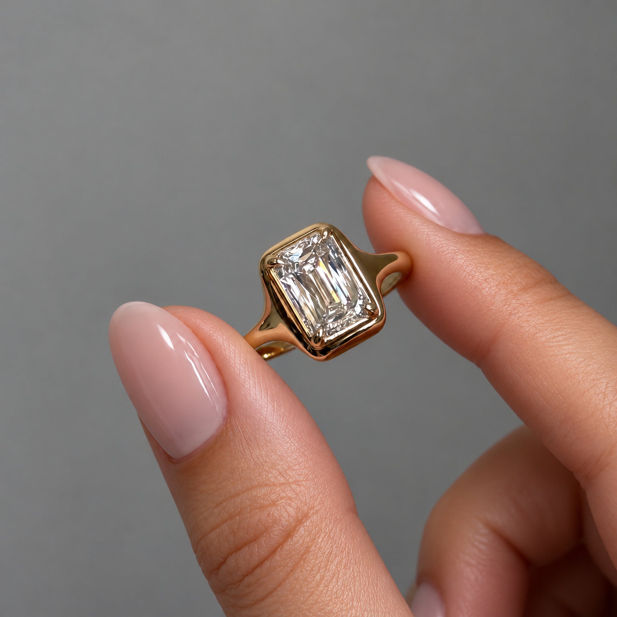 3 ct Emerald-Cut Moissanite Bezel-Prong Ring in yellow gold vermeil, held between two fingers.