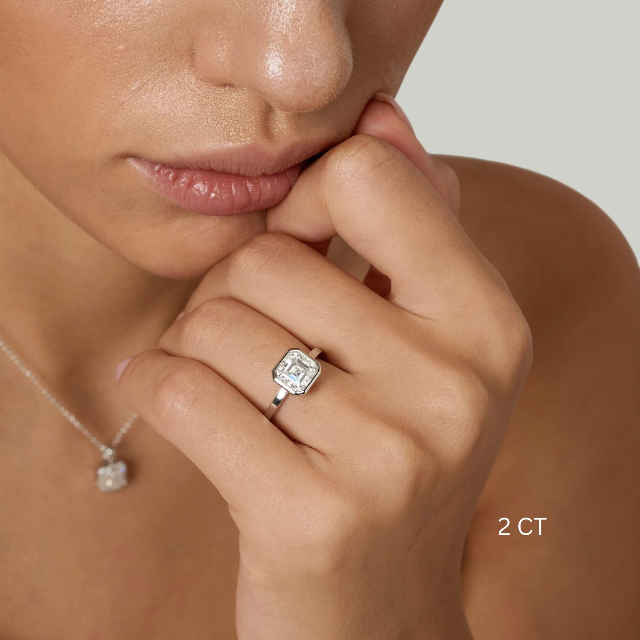Asscher-cut moissanite bezel solitaire ring worn on a finger with a 2 ct size label.