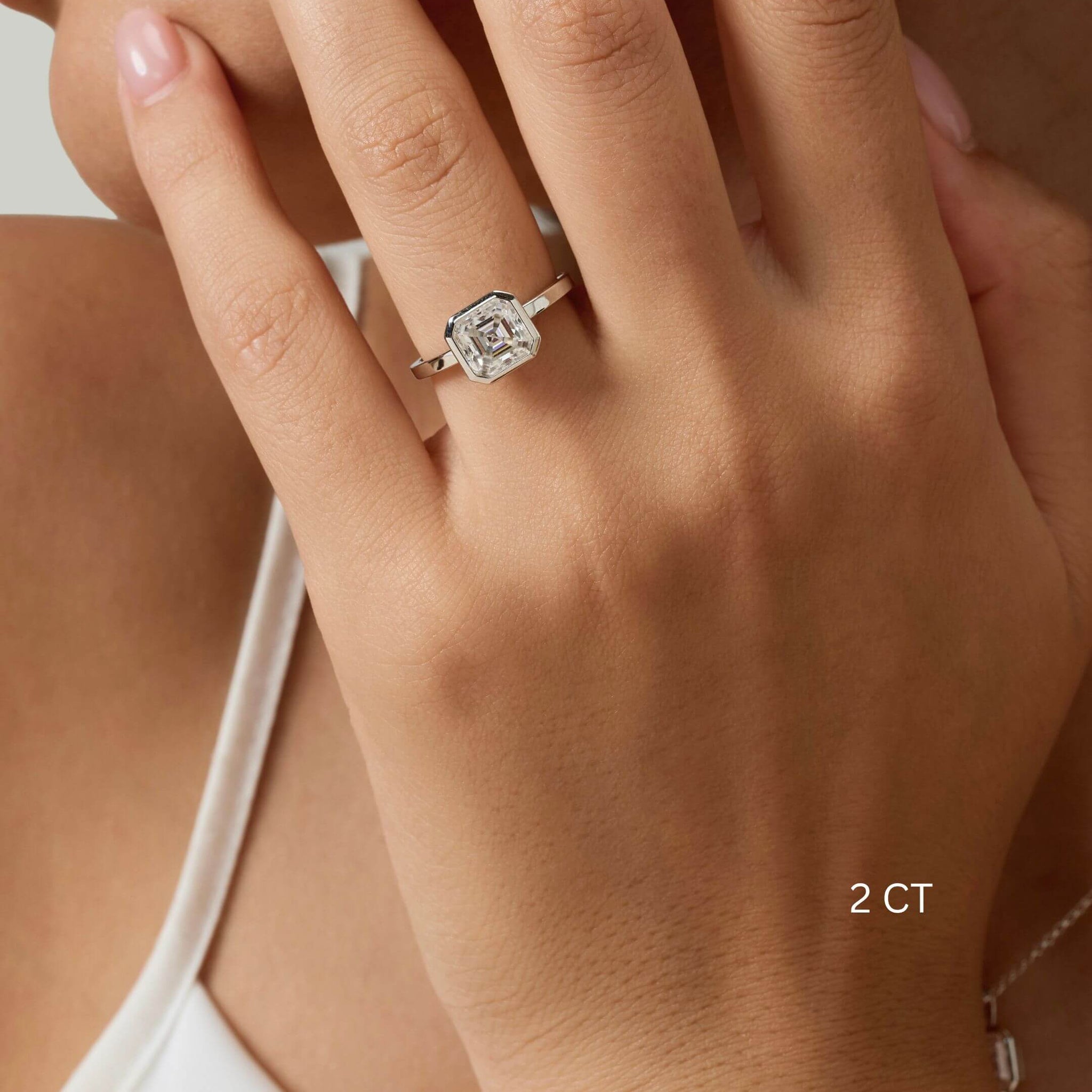 Asscher-cut moissanite bezel solitaire ring worn on a finger with a 2 ct size label.