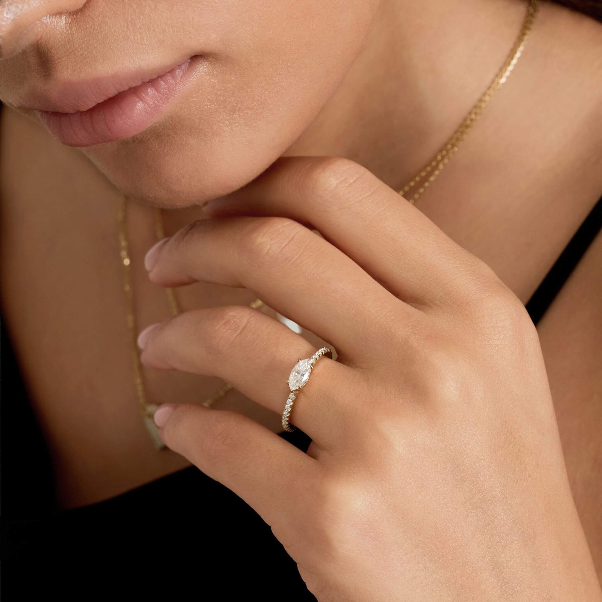 East-west marquise-cut moissanite solitaire ring with pavé band worn on a finger.