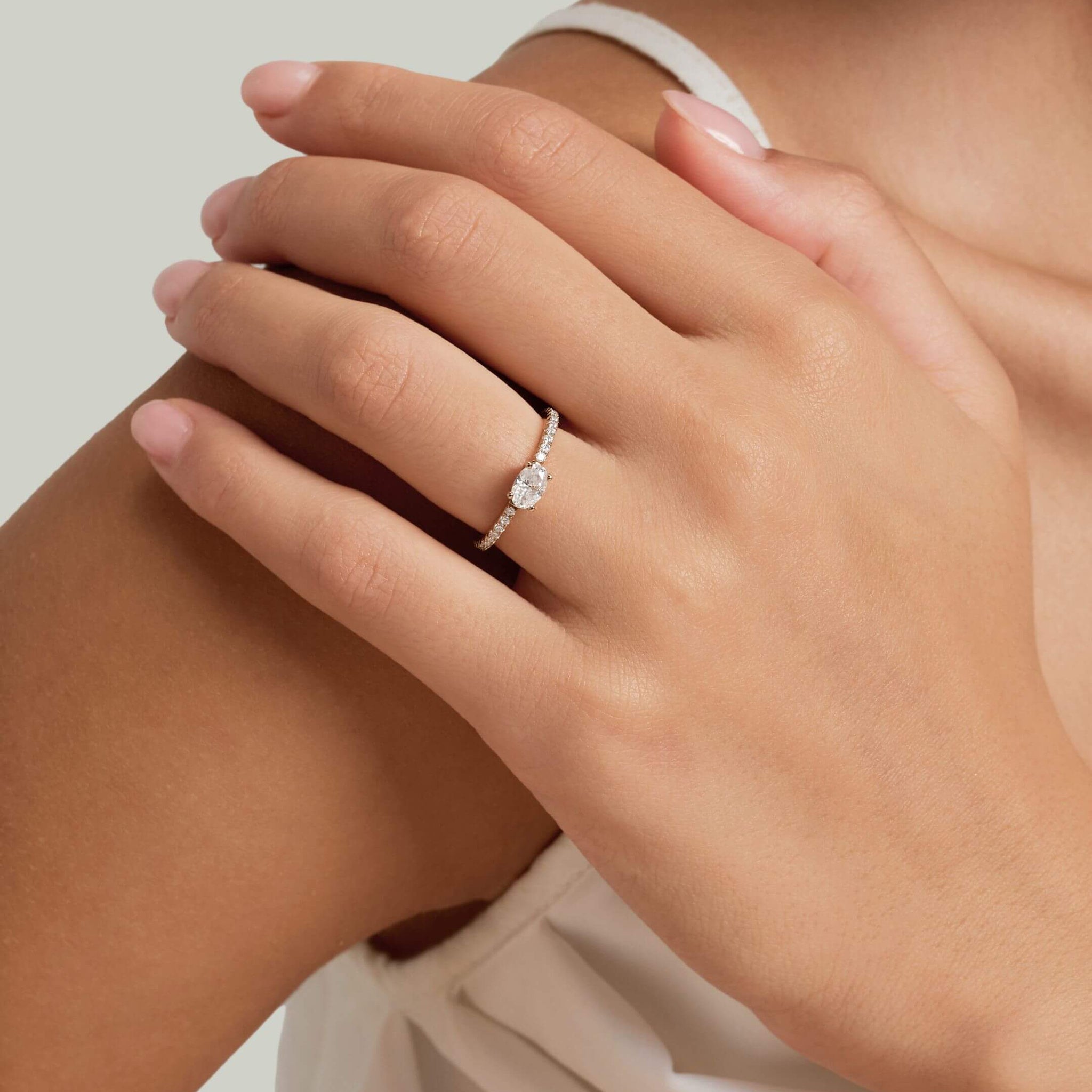 East-west oval-cut moissanite solitaire ring with pavé band worn on a finger.