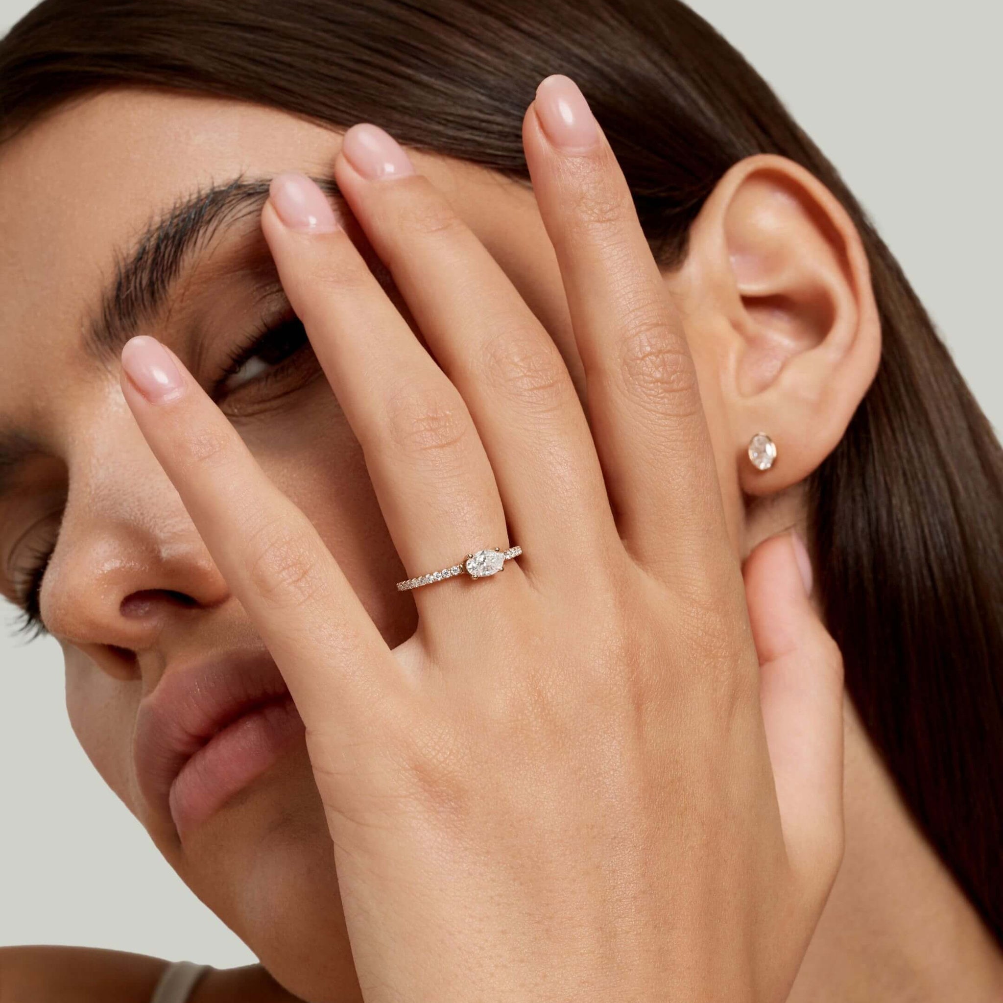 East-west oval-cut moissanite solitaire ring with pavé band worn on a finger.