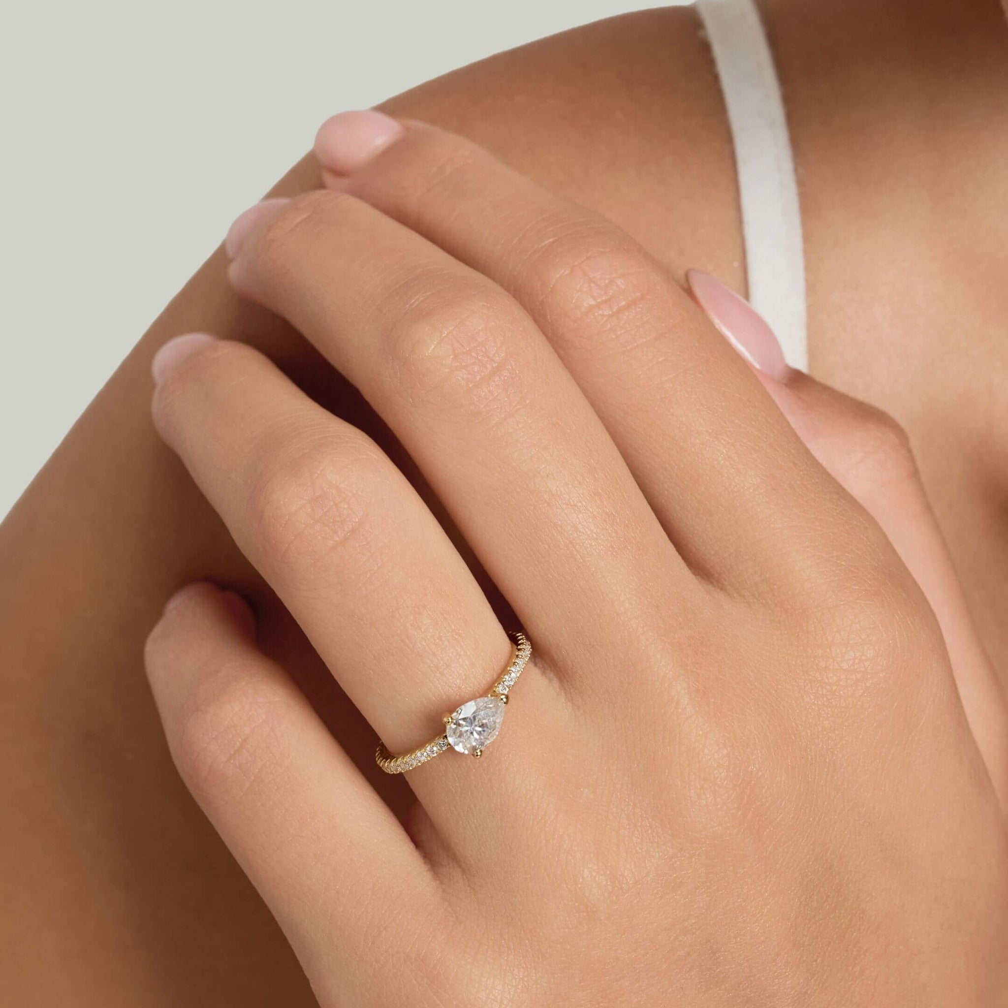 East-west pear-cut moissanite solitaire ring with pavé band worn on a finger.