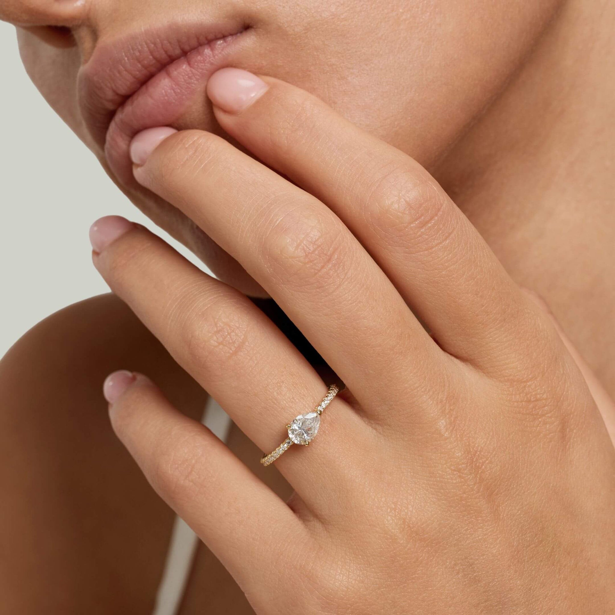 East-west pear-cut moissanite solitaire ring with pavé band worn on a finger.