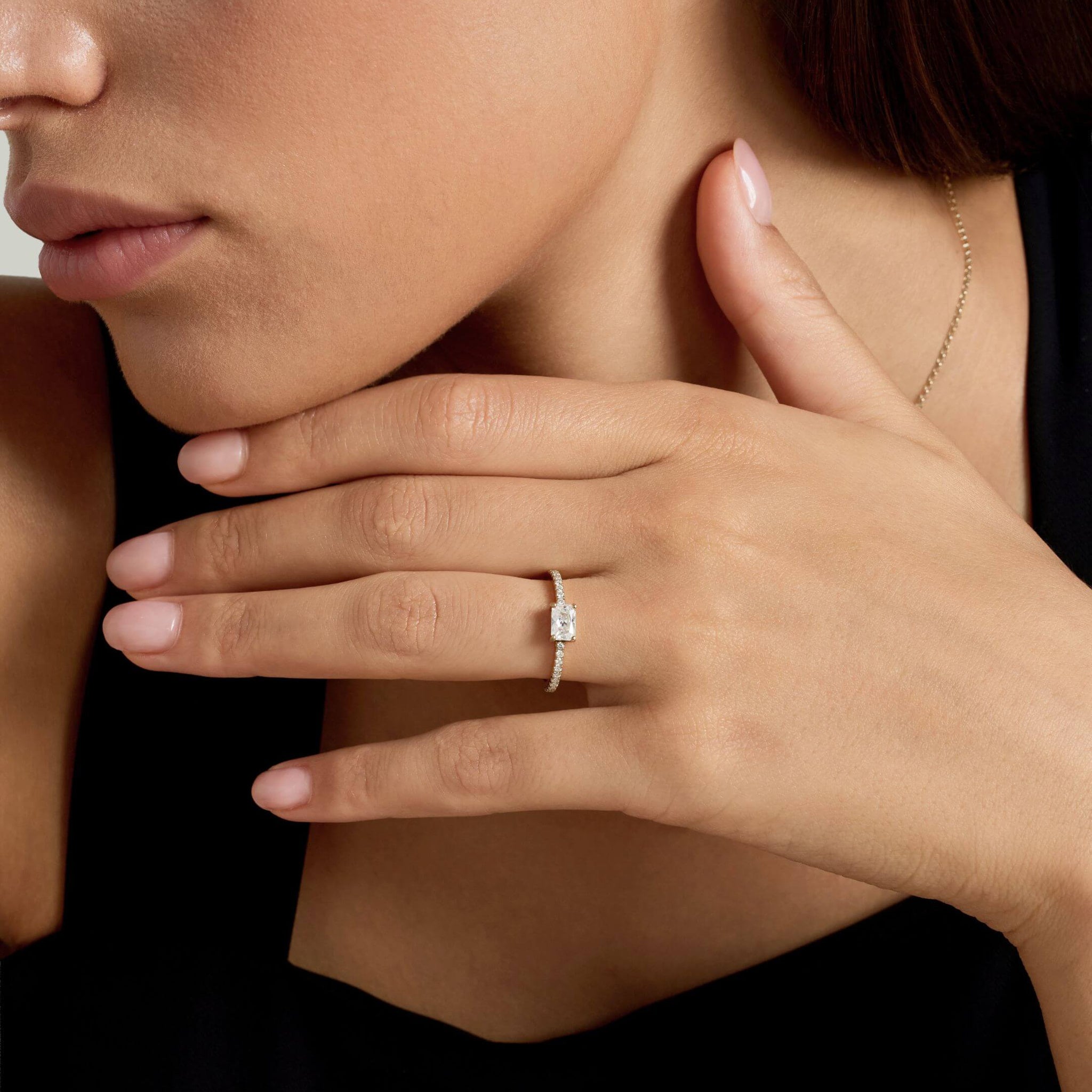 East-west radiant-cut moissanite solitaire ring with pavé band worn on a finger.