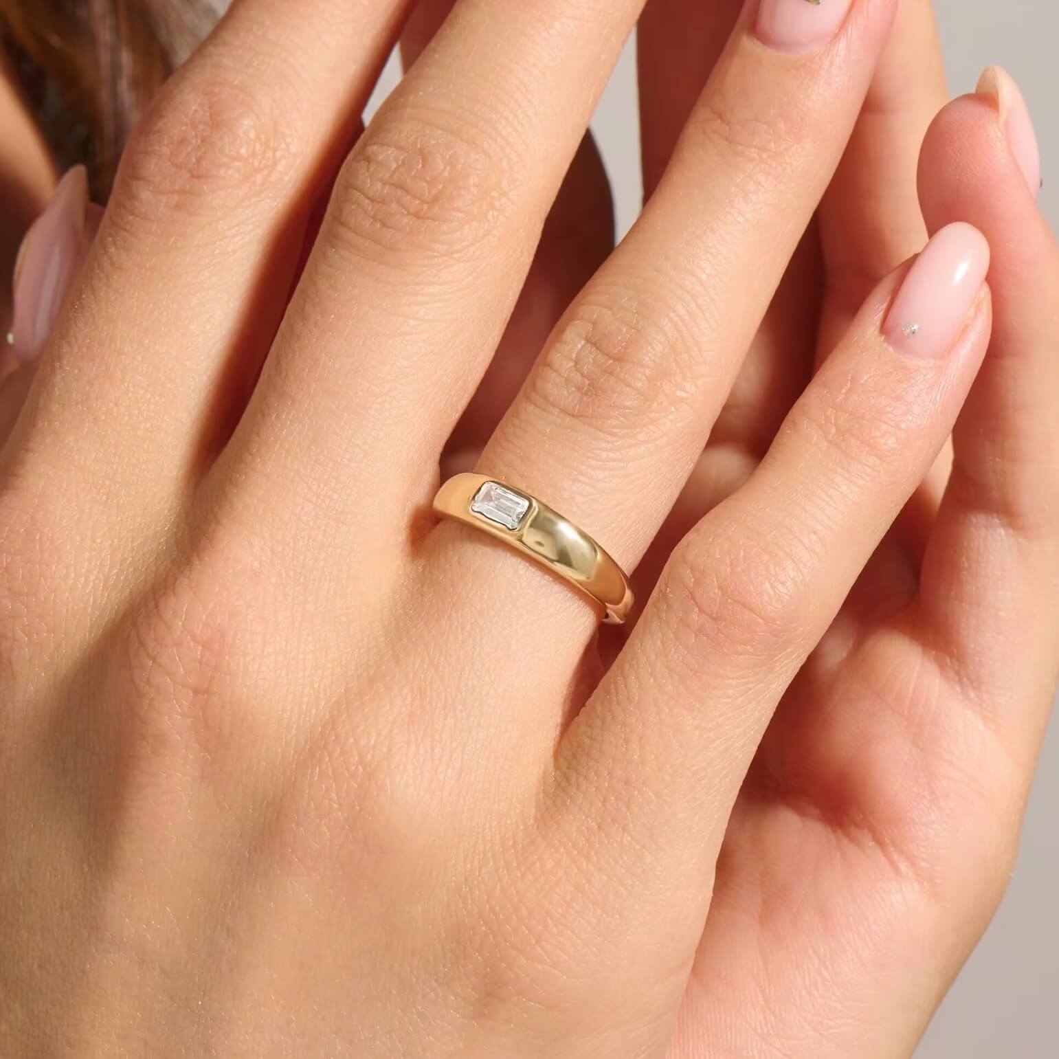Emerald-cut moissanite bezel dome ring worn on a finger.