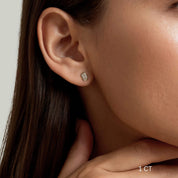 Emerald-cut moissanite bezel stud earrings worn on the ear with a 1 ct size label.