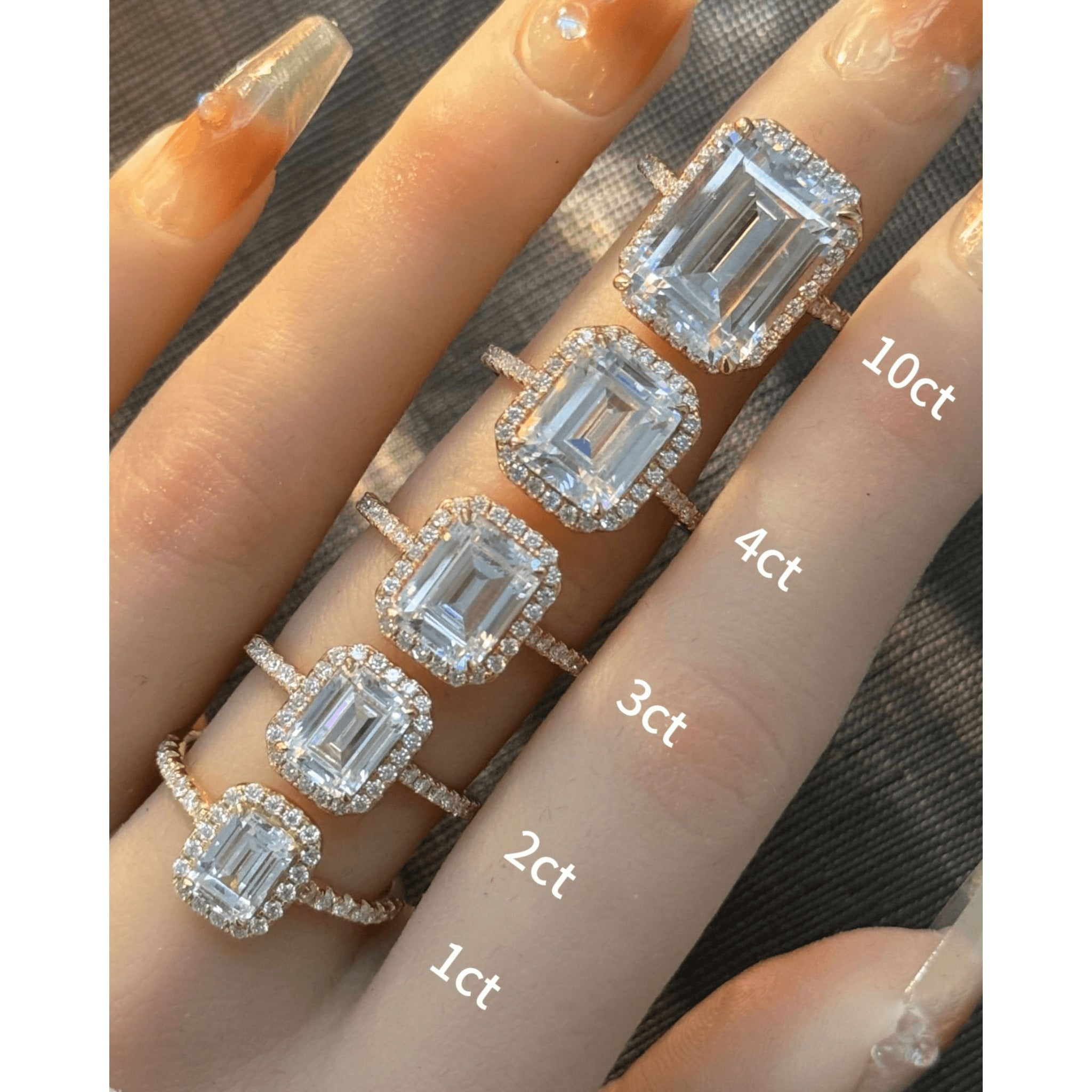 Emerald-cut moissanite halo ring with pavé band rings arranged across fingers for a carat-size comparison.