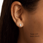 Emerald-cut moissanite stud earrings worn on the ear, 1 ct per pair with 0.5 ct per stone.
