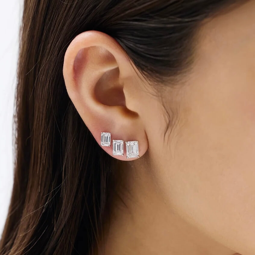 Emerald-cut moissanite stud earrings different stud sizes shown together on the ear.