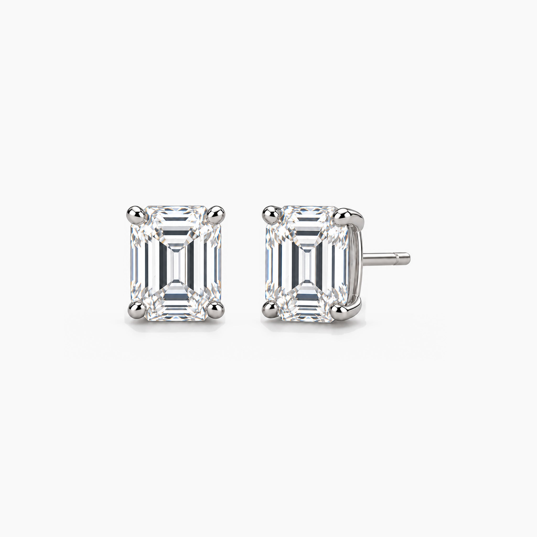 Emerald-cut moissanite stud earrings in white gold vermeil, front and three-quarter views.