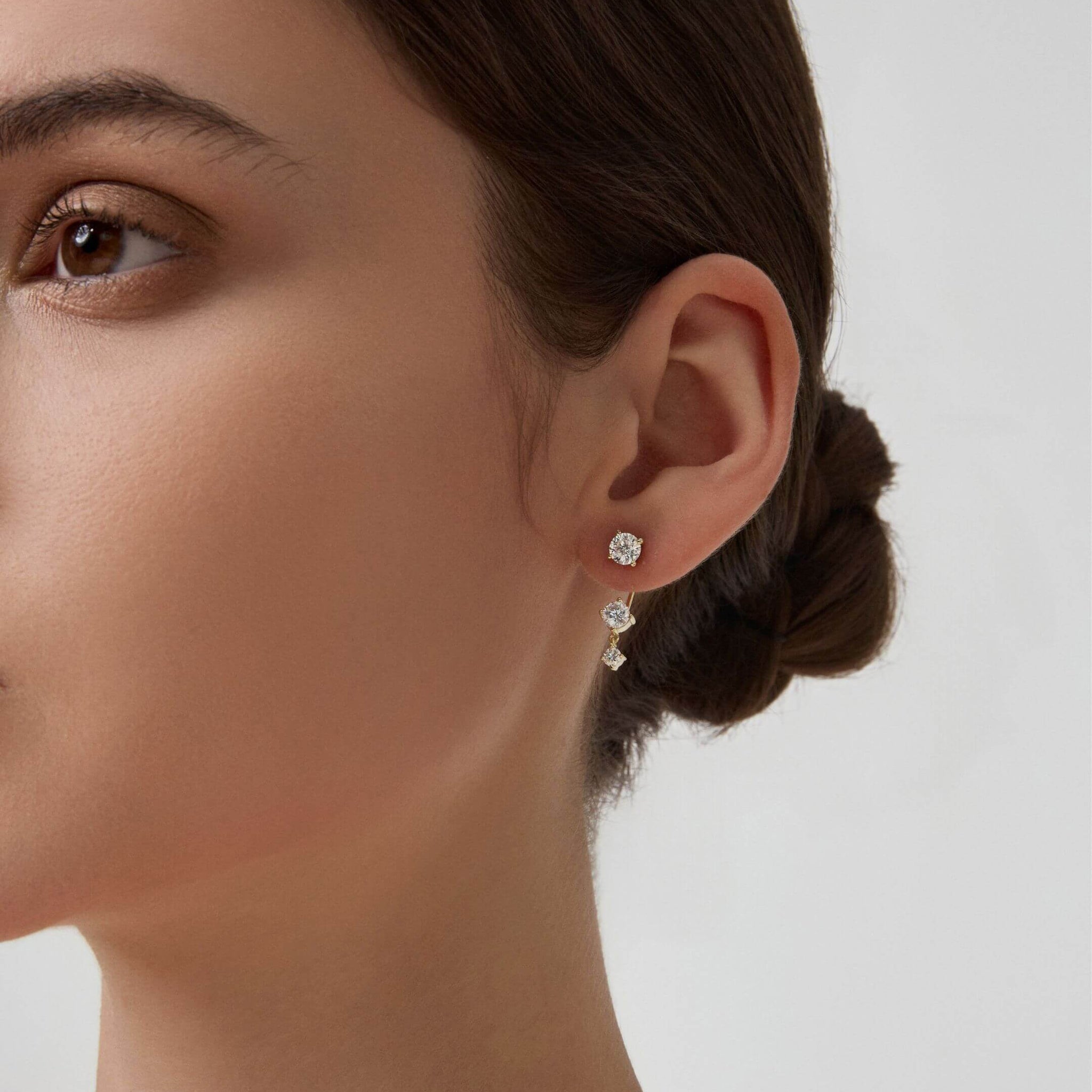 Floating three-stone moissanite drop earrings worn on the ear.