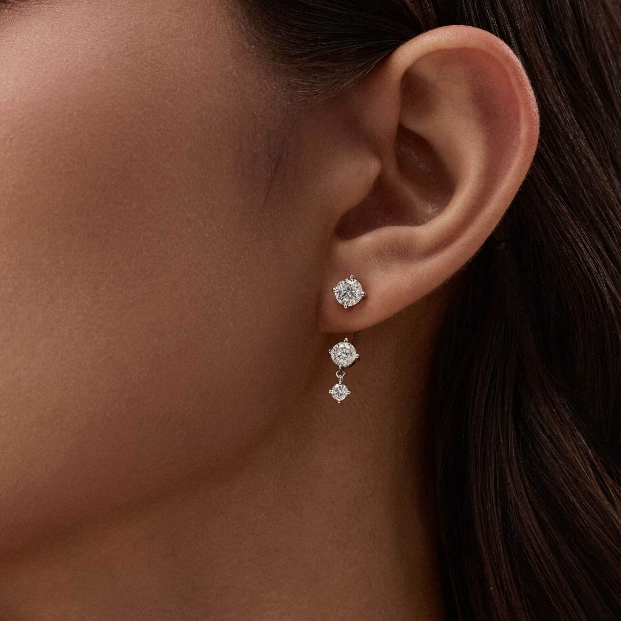 Floating three-stone moissanite drop earrings worn on the ear.