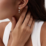 Floating three-stone moissanite drop earrings worn on the ear.