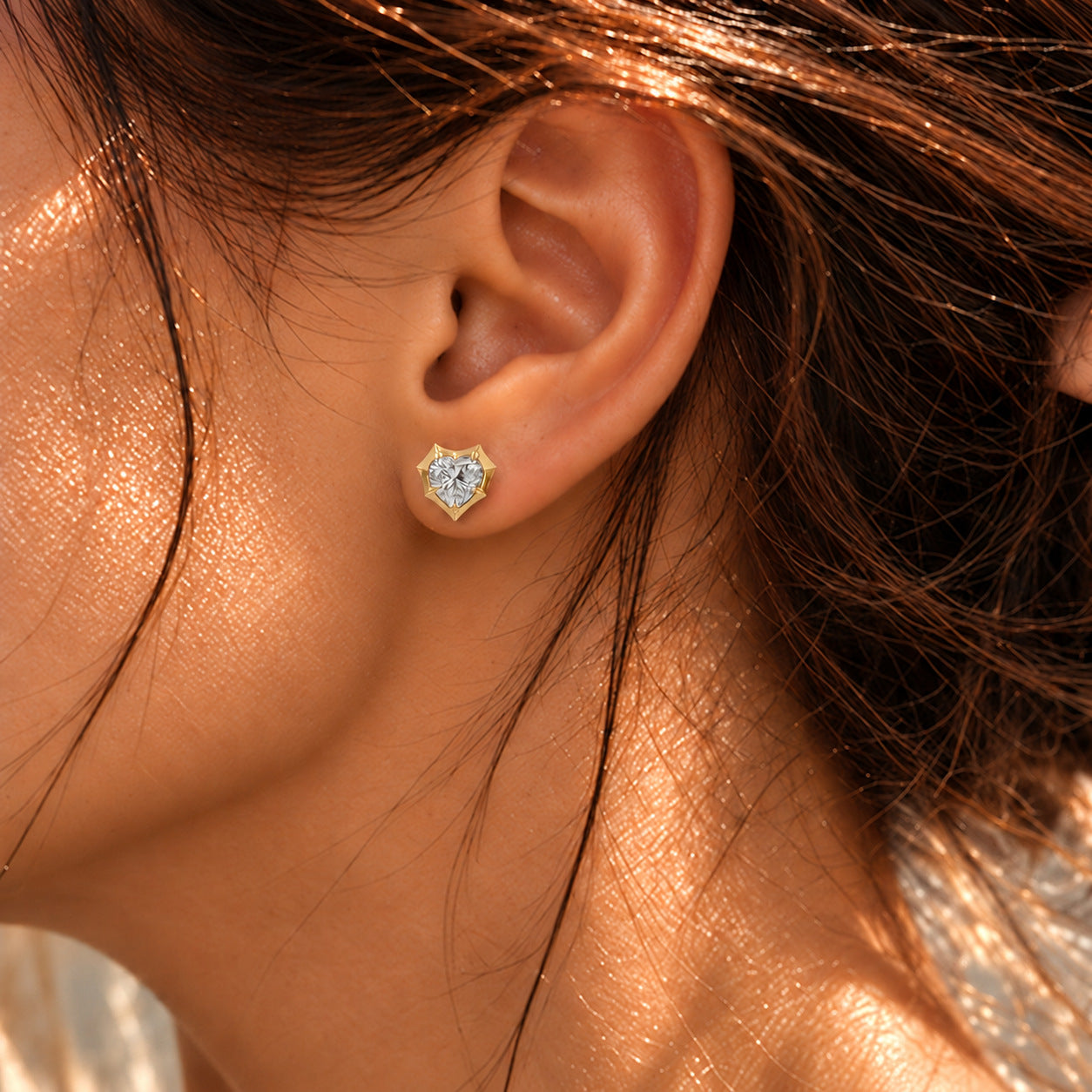 Close-up of a model wearing a heart-cut moissanite bezel-prong stud earring in 18k yellow gold vermeil.
