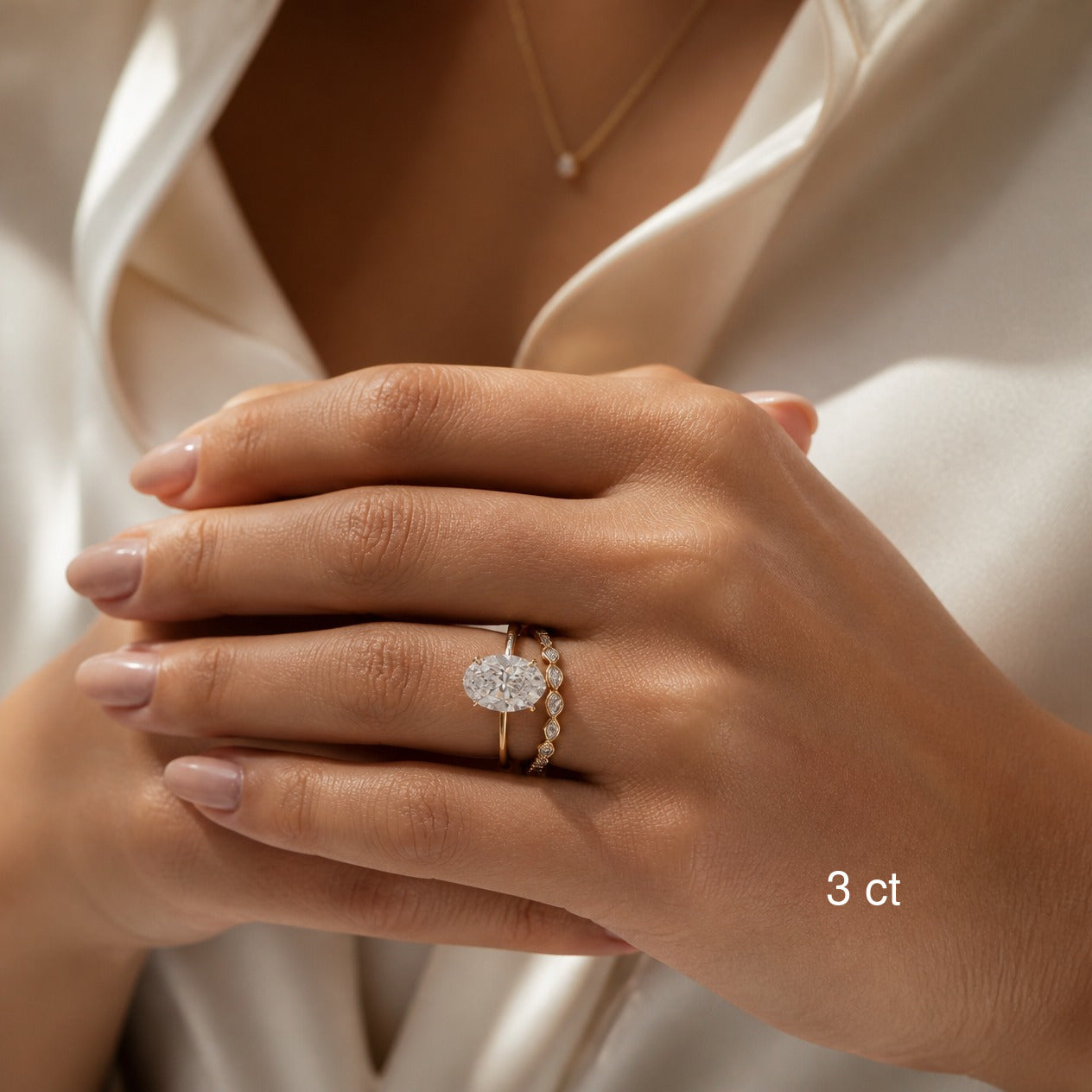 3 ct oval-cut moissanite ring in yellow gold worn with a stacking band.
