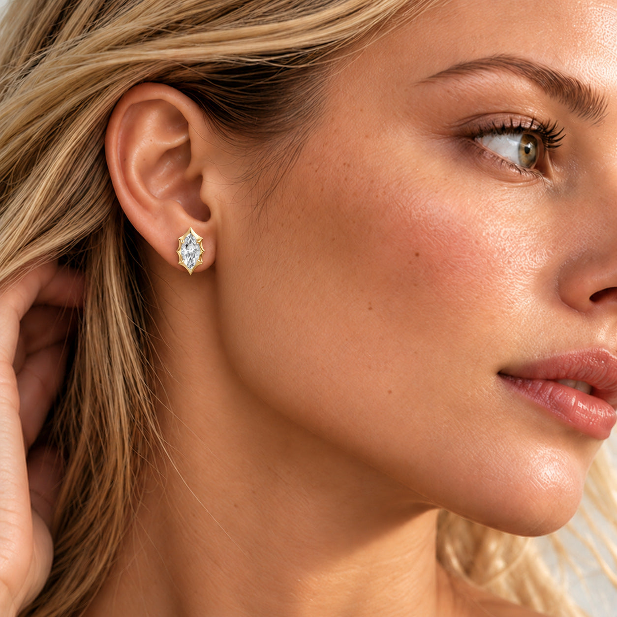 Close-up of a model wearing a marquise-cut moissanite bezel-prong stud earring in 18k yellow gold vermeil.