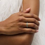 Moissanite and lab-grown emerald eternity ring worn on a finger.