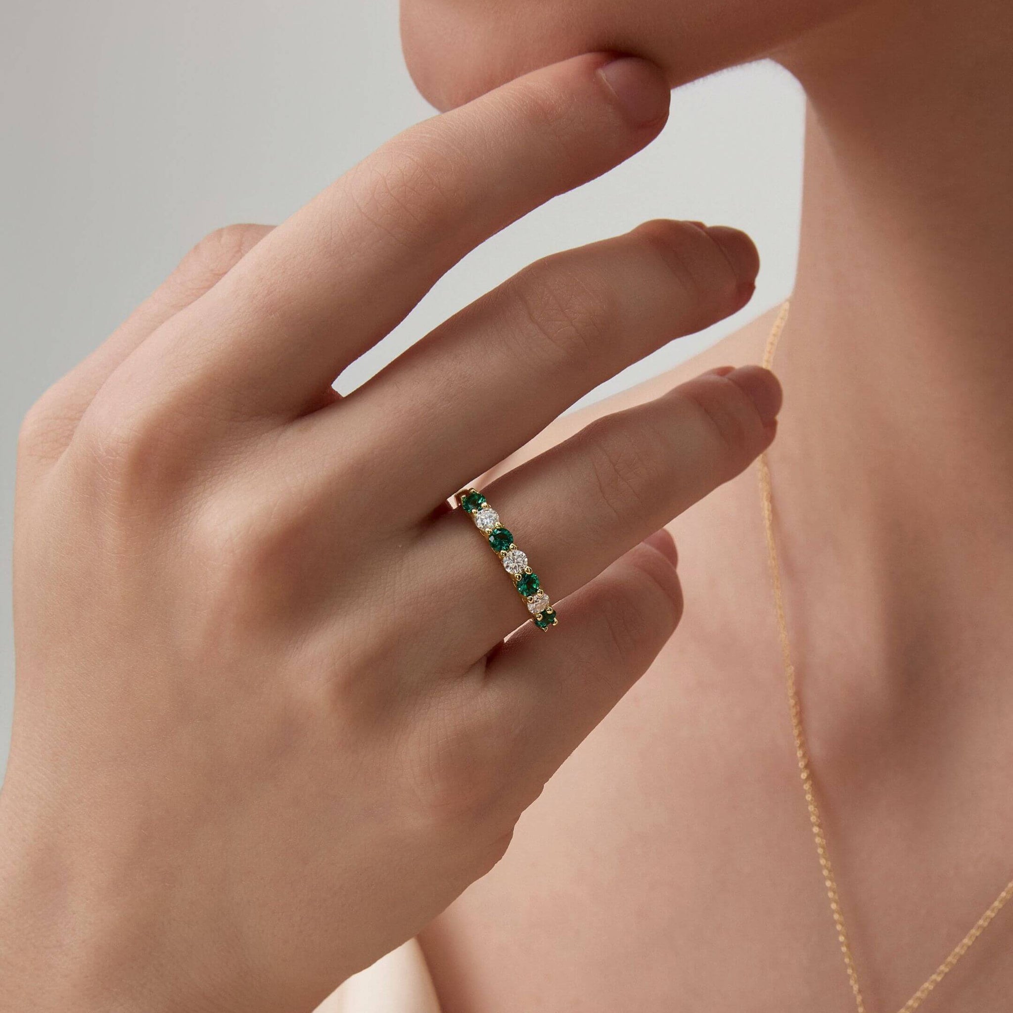 Moissanite and lab-grown emerald half eternity ring worn on a finger.