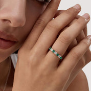 Moissanite and lab-grown emerald half eternity ring worn on a finger.