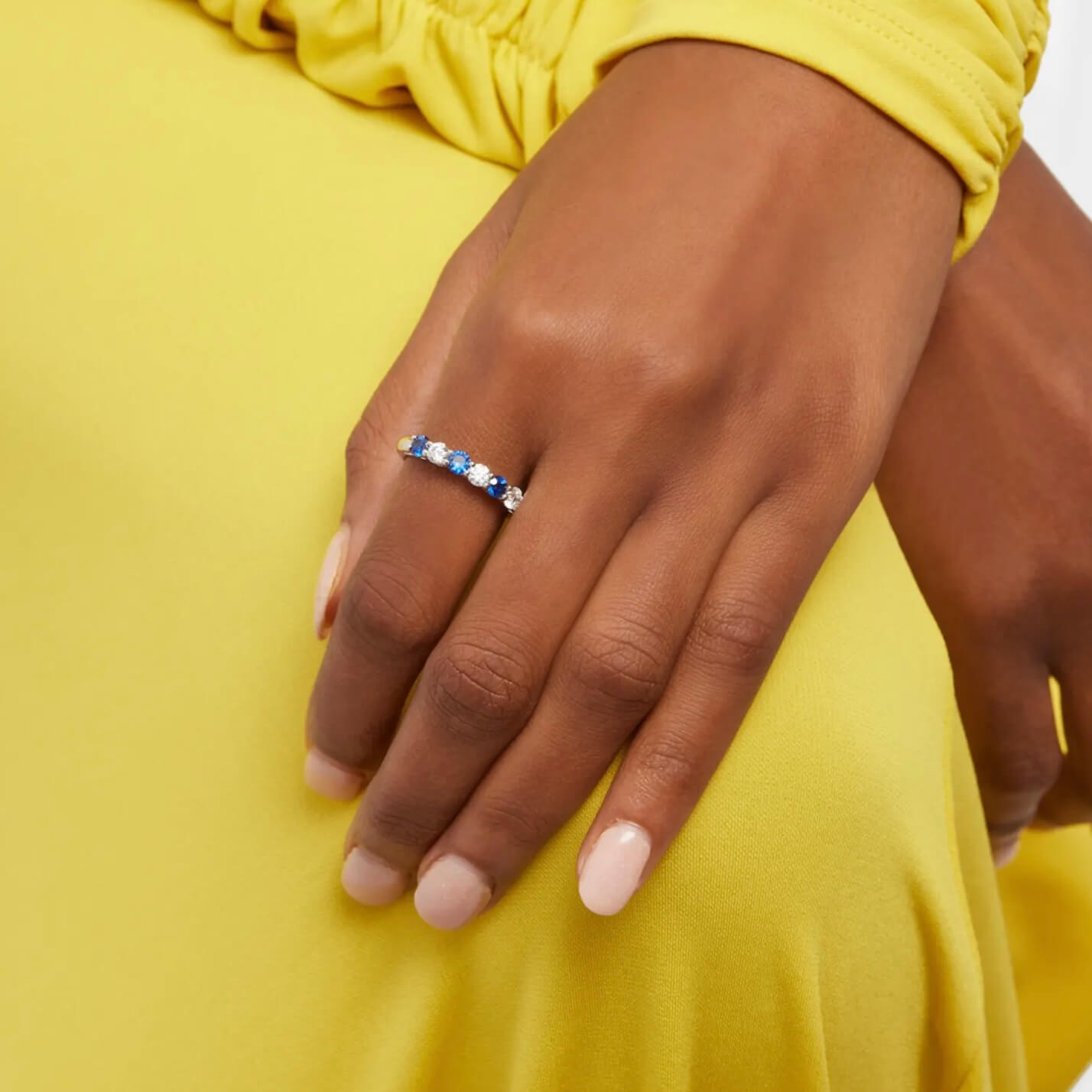 Moissanite and lab-grown sapphire half eternity ring worn on a finger.
