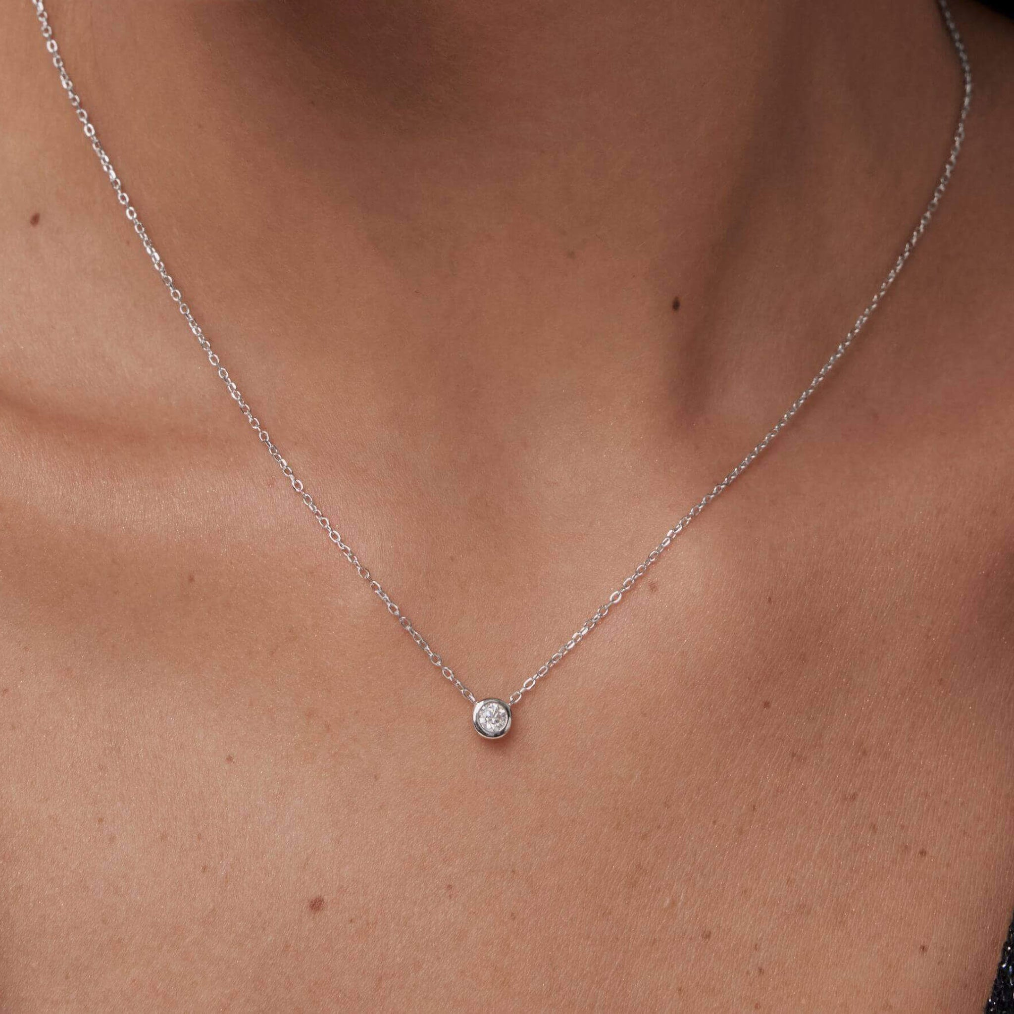 Moissanite bezel pendant necklace worn at the neckline.