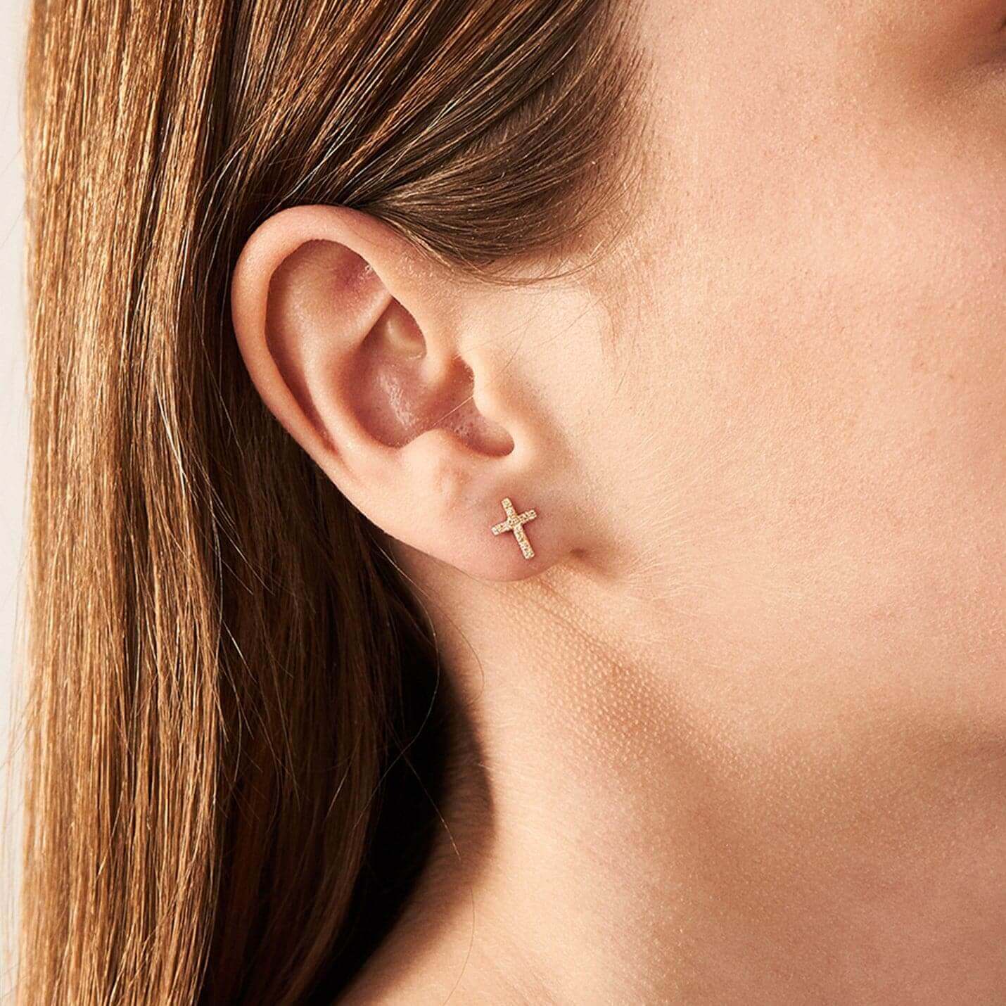 Moissanite cross stud earrings worn on the ear.