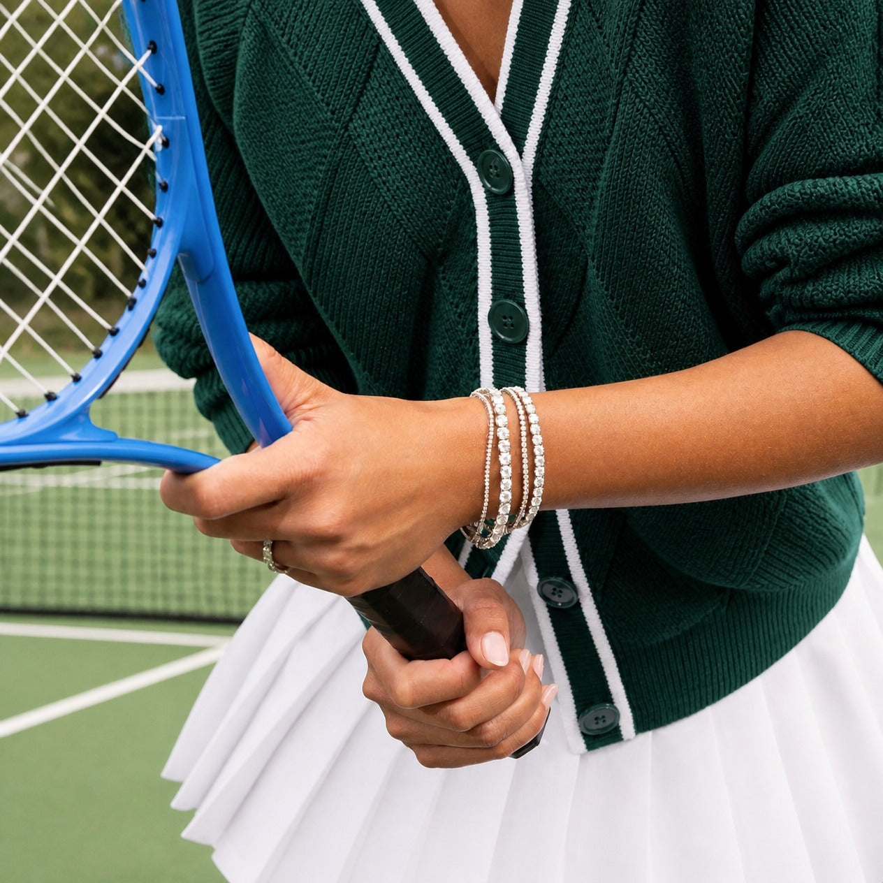 White gold moissanite tennis bracelets in mixed widths stacked on a wrist, styled with a green tennis cardigan.