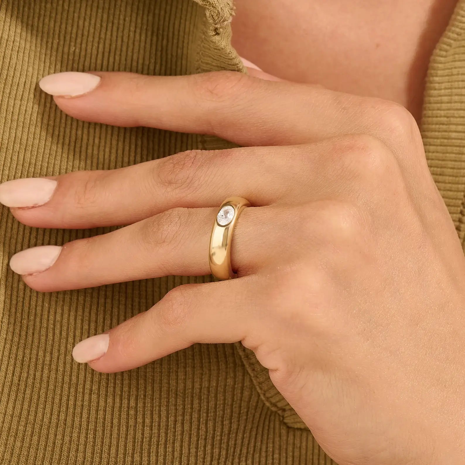 Oval-cut moissanite bezel dome ring worn on a finger.
