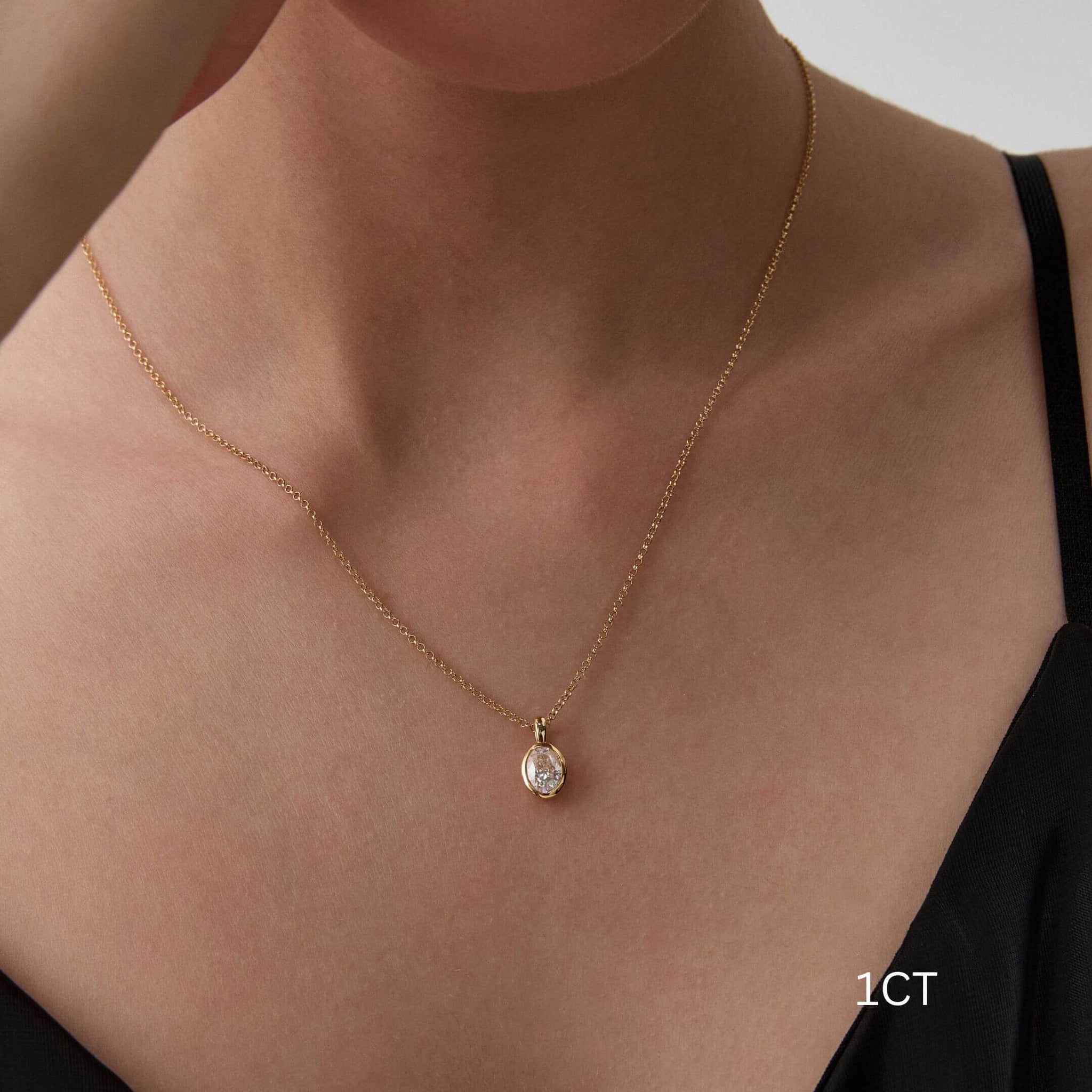 Oval-cut moissanite bezel pendant necklace worn at the neckline.