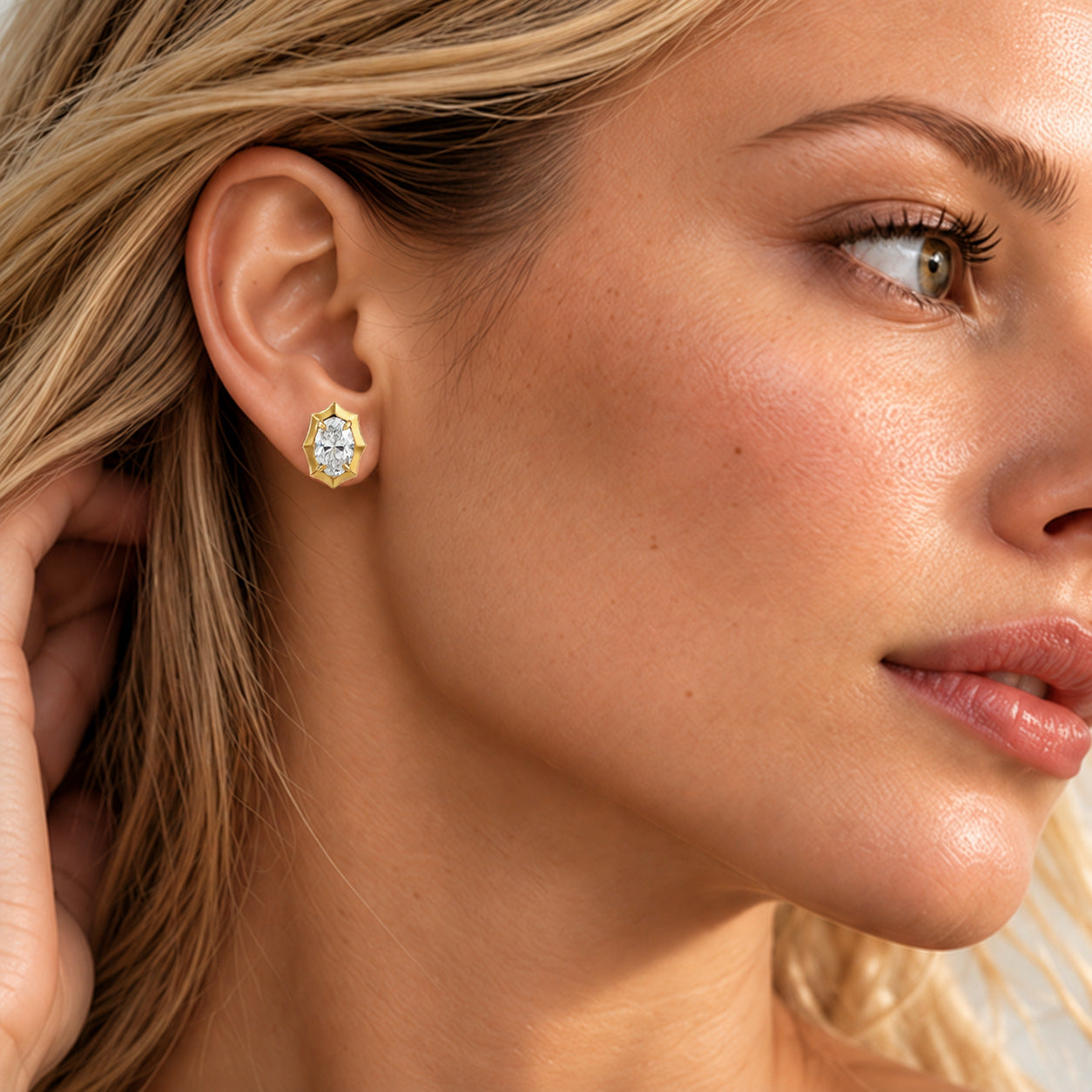 Close-up of a model wearing an oval-cut moissanite bezel-prong stud earring in 18k yellow gold vermeil.