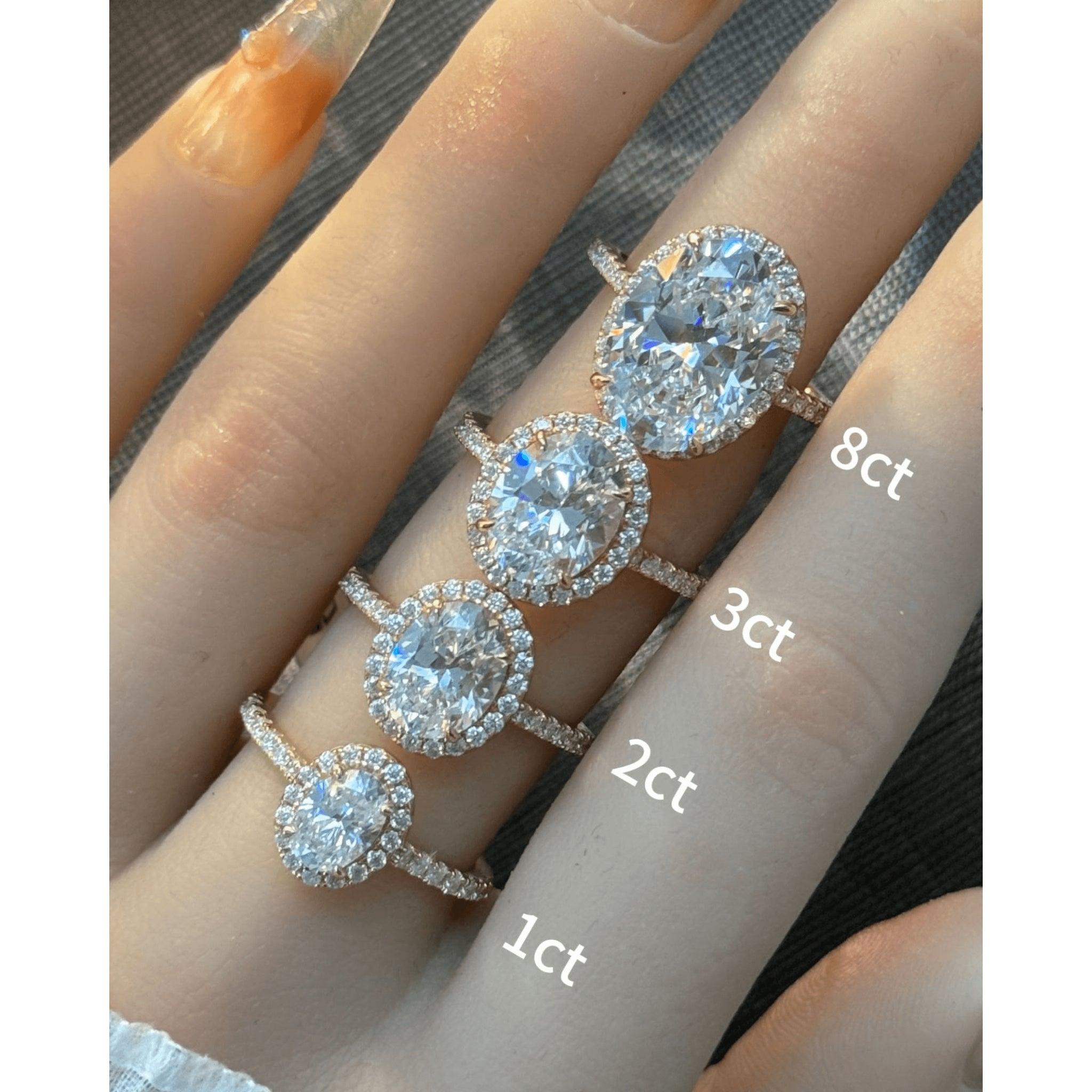 Oval-cut moissanite halo ring with pavé band rings arranged across fingers for a carat-size comparison.