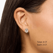 Oval-cut moissanite stud earrings worn on the ear, 4 ct per pair with 2 ct per stone.