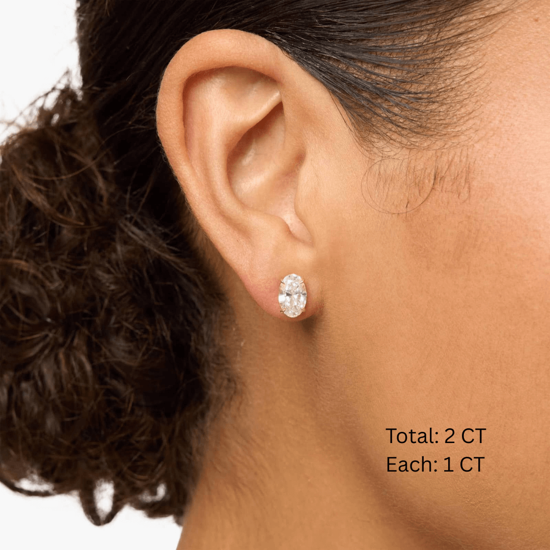 Oval-cut moissanite stud earrings worn on the ear, 2 ct per pair with 1 ct per stone.