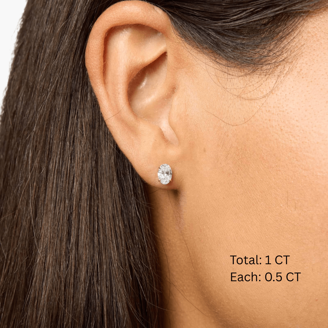 Oval-cut moissanite stud earrings worn on the ear, 1 ct per pair with 0.5 ct per stone.