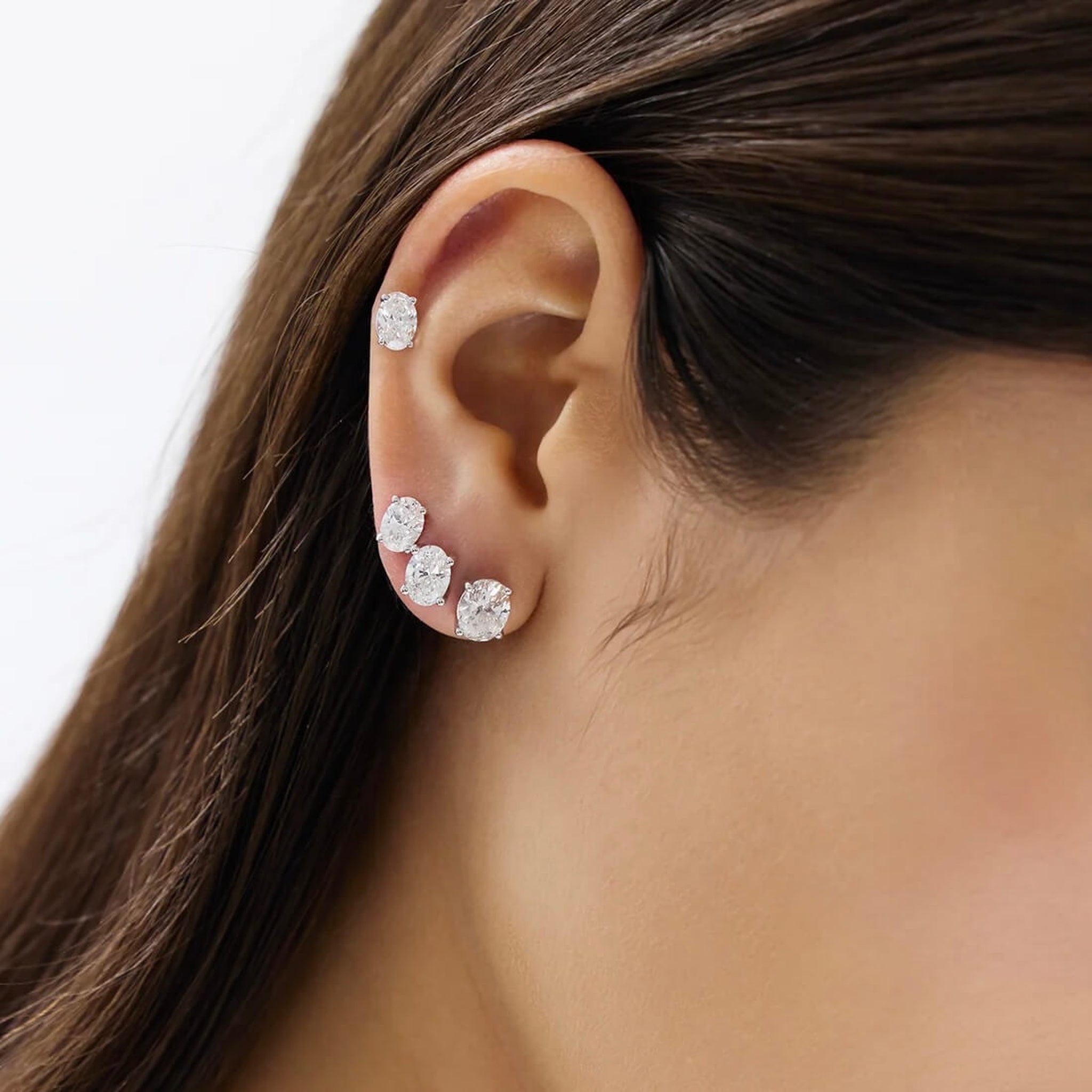 Oval-cut moissanite stud earrings different stud sizes shown together on the ear.
