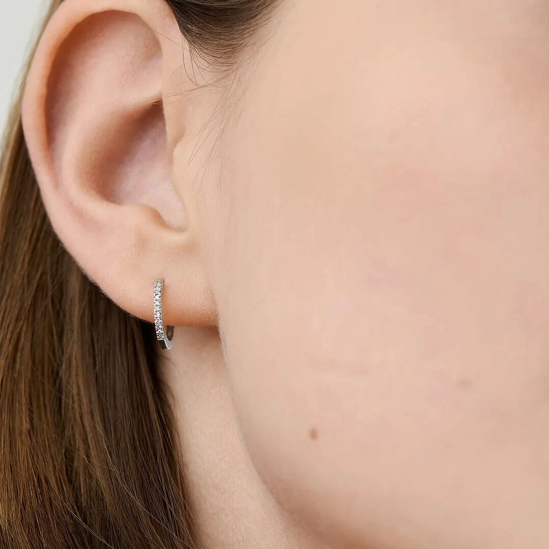 Pavé moissanite huggie hoop earrings worn on the ear.