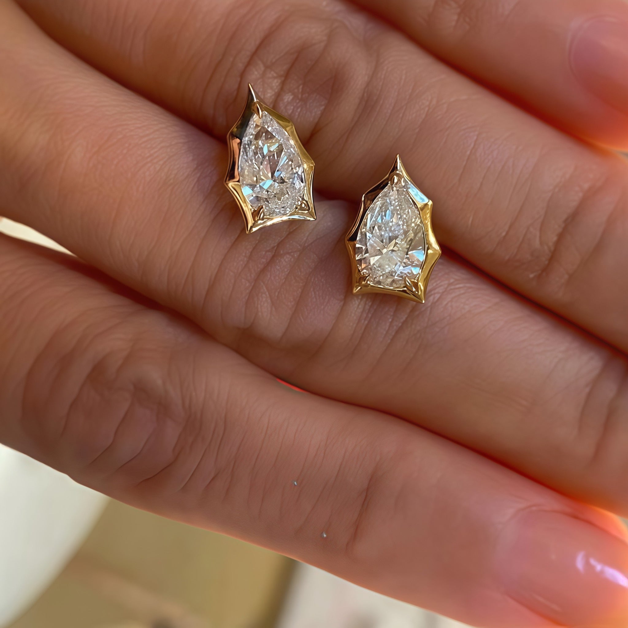 Hand detail of a pair of pear-cut moissanite bezel-prong stud earrings in 18k yellow gold vermeil