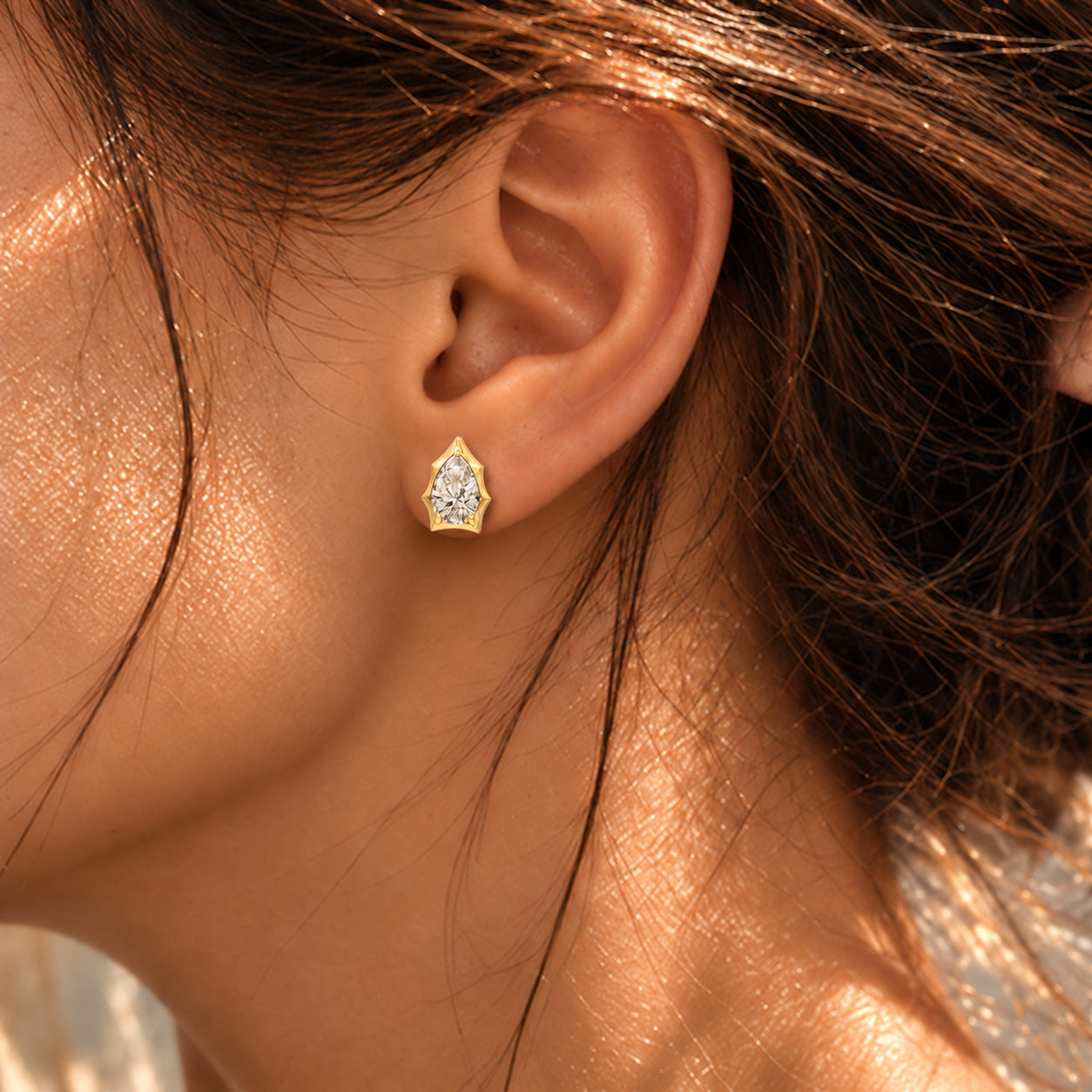 Close-up of a model wearing a pear-cut moissanite bezel-prong stud earring in 18k yellow gold vermeil.
