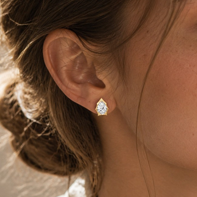 Pear-cut moissanite bezel-prong stud earrings in yellow gold vermeil, ear close-up.