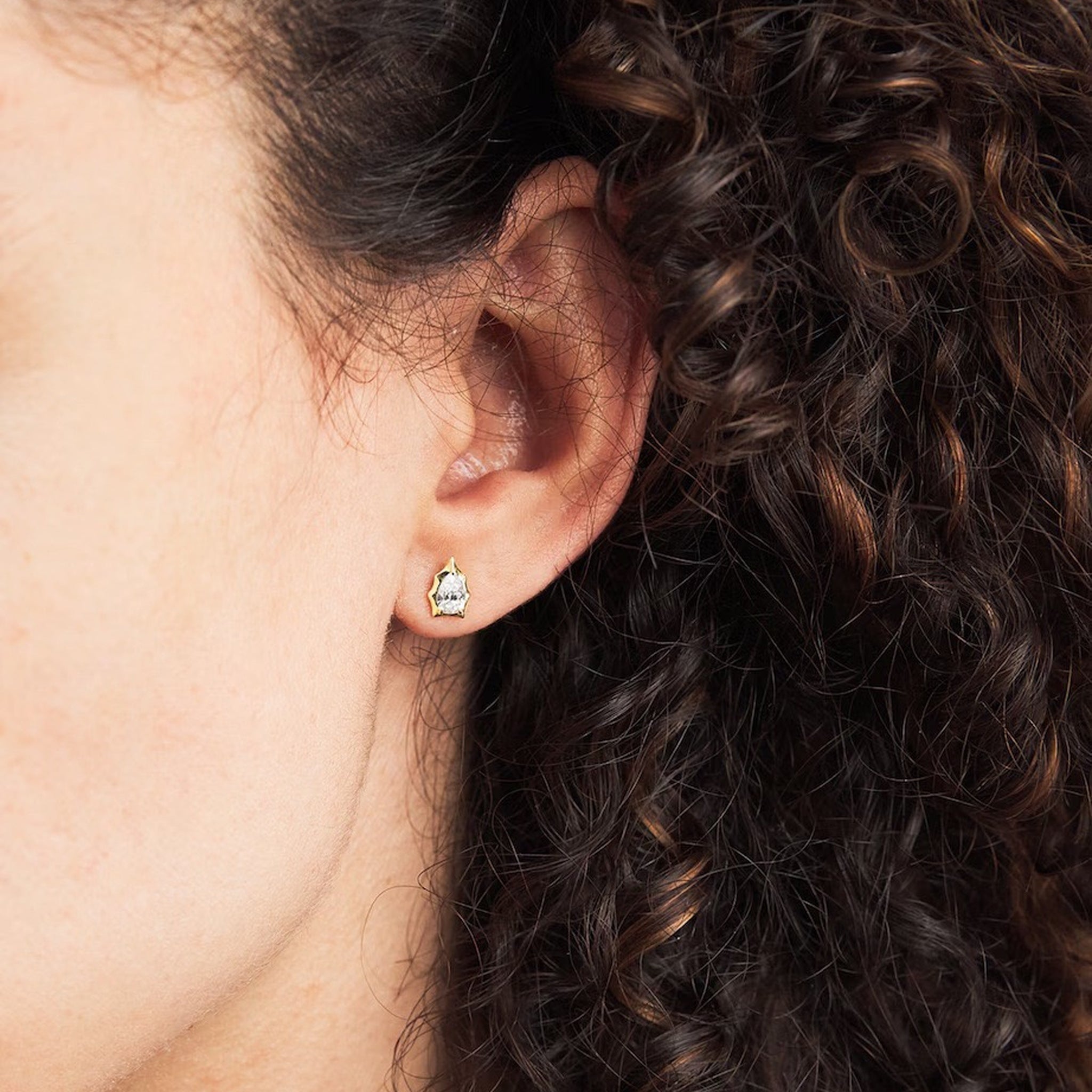 Model wearing pear-cut moissanite bezel-prong stud earrings in 18k yellow gold vermeil