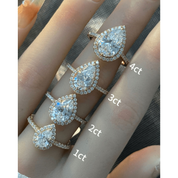 Pear-cut moissanite halo ring with pavé band rings arranged across fingers for a carat-size comparison.